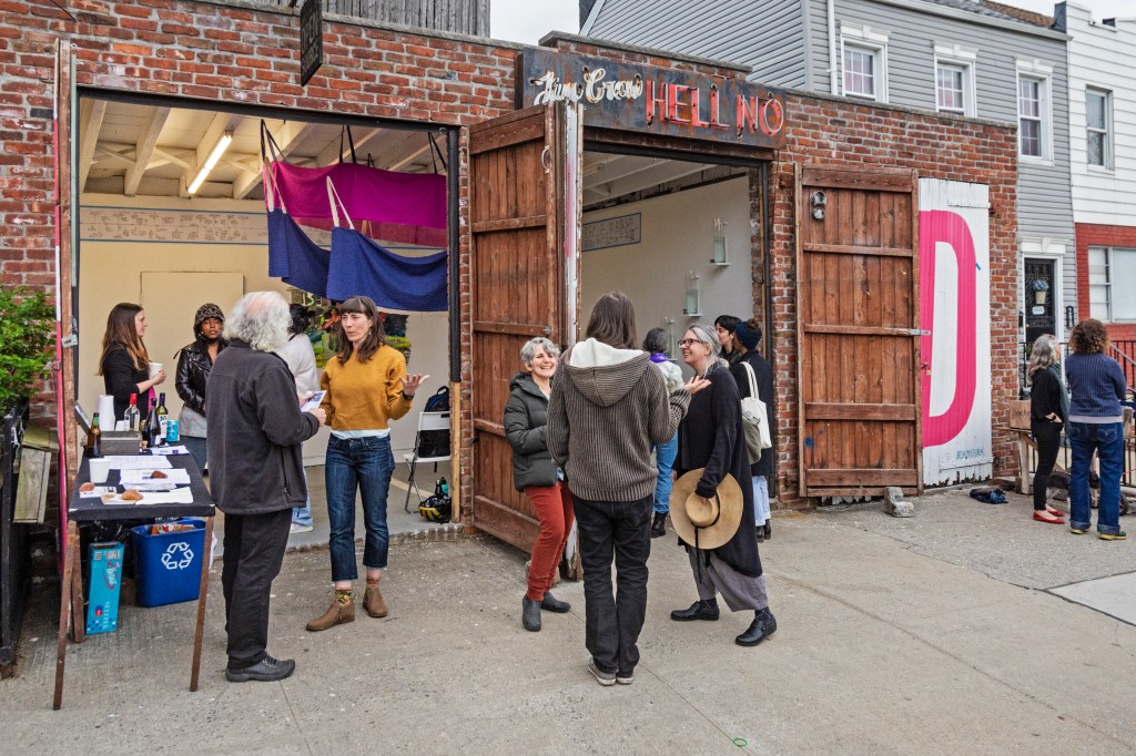 Open Source Gallery seen from the outside, with two open doors. Visible through the doors are glimpses oof the exhibition, and several people standing inside and outside the gallery